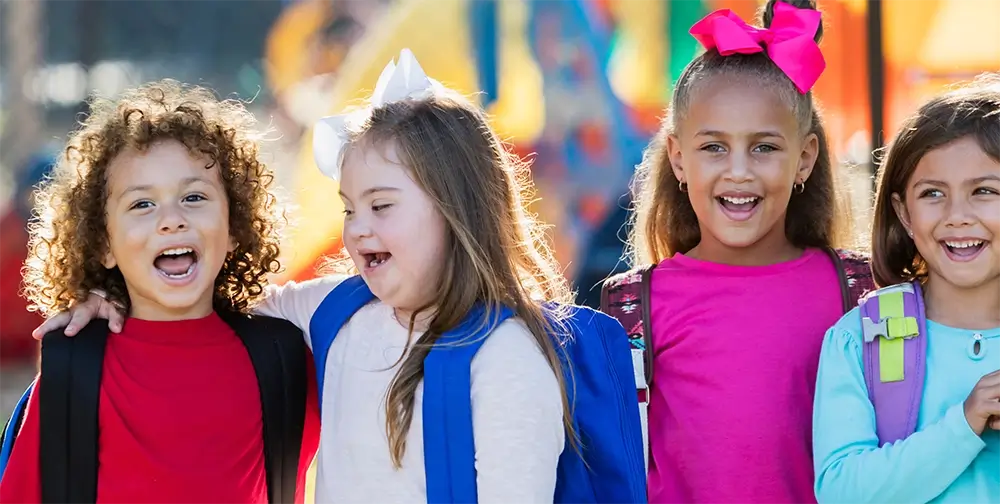 Four smiling children outside wearing rucksacks and colourful clothing
